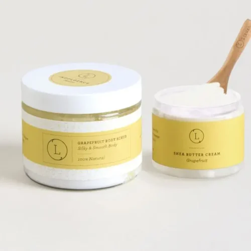 Reviving skincare set with grapefruit body scrub and nourishing shea butter cream, displayed on white table and whiter bsckground. Shea Butter Cream opened with small wooden spoon inserted. Perfect for exfoliating and hydrating dry skin.