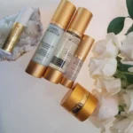 Collagen Anti-Aging Set by Adriana Catano featuring serum, moisturizer, and eye cream designed to reduce fine lines, firm skin, and boost collagen for a youthful glow. Displayed against a soft pink background with white roses.