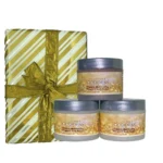 Organic shimmering whipped body butter trio in three jars, with natural ingredients like shea butter and coconut oil, perfect for deep hydration and glowing skin. displayed in front of white background alongside a gift wrapped package.
