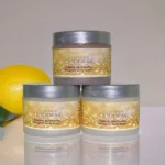 Organic shimmering whipped body butter trio in three jars, displayed on a wooden surface with natural ingredients like shea butter and coconut oil, perfect for deep hydration and glowing skin. Displayed with a lemon in the background.