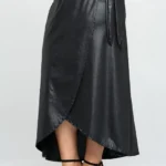 Closeup of side view of Model wearing a chic faux leather maxi wrap skirt with a high waist and side tie detail, showcasing a sleek, elegant look perfect for modern street style or evening wear.