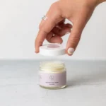 Close up of woman lifting lid from lavender shea butter moisturizing cream