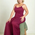 Plus size model seated on a stool wearing a button front wide leg jumpsuit, featuring a relaxed fit, flowy wide leg silhouette, and flattering design styled for a chic and confident look