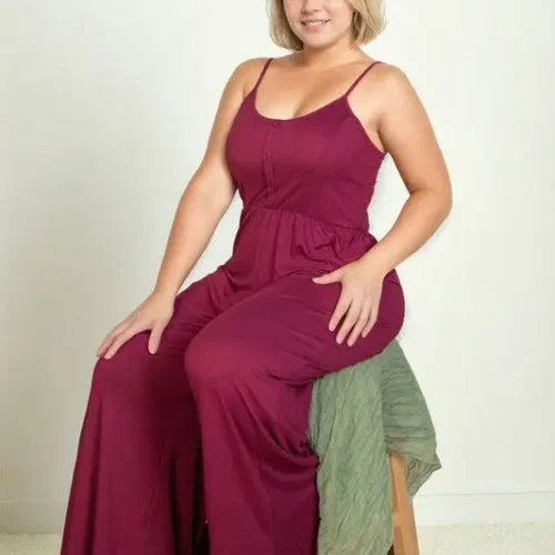 Plus size model seated on a stool wearing a button front wide leg jumpsuit, featuring a relaxed fit, flowy wide leg silhouette, and flattering design styled for a chic and confident look